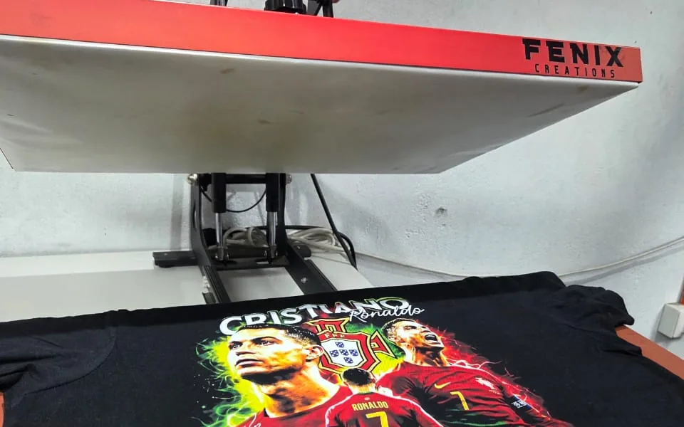 Prensa térmica de Fénix Creations con una polera negra recién estampada a todo color