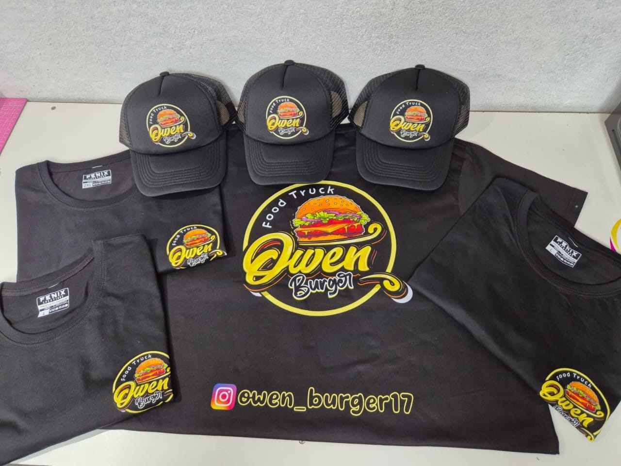 Poleras negras y jockeys trucker con el logo de Food Truck Owen Burger estampado en amarillo.