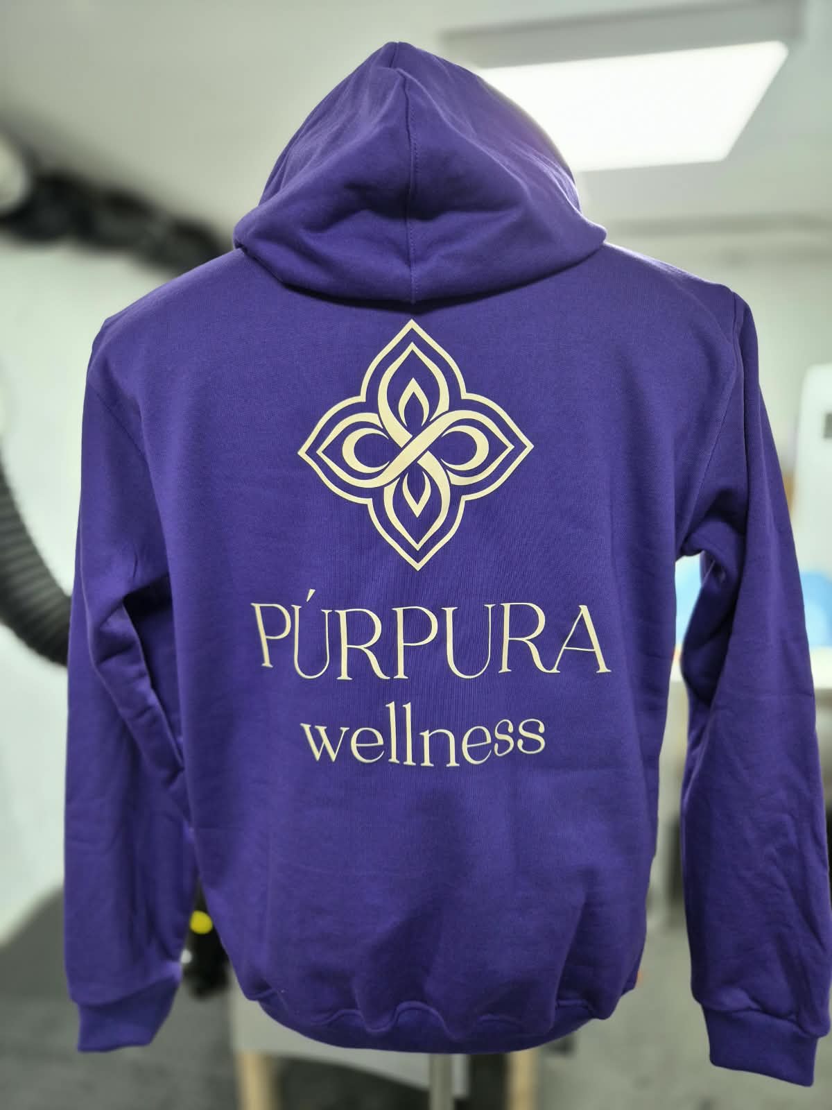 Polerón morado con el logo Púrpura Wellness estampado en dorado en toda la espalda.